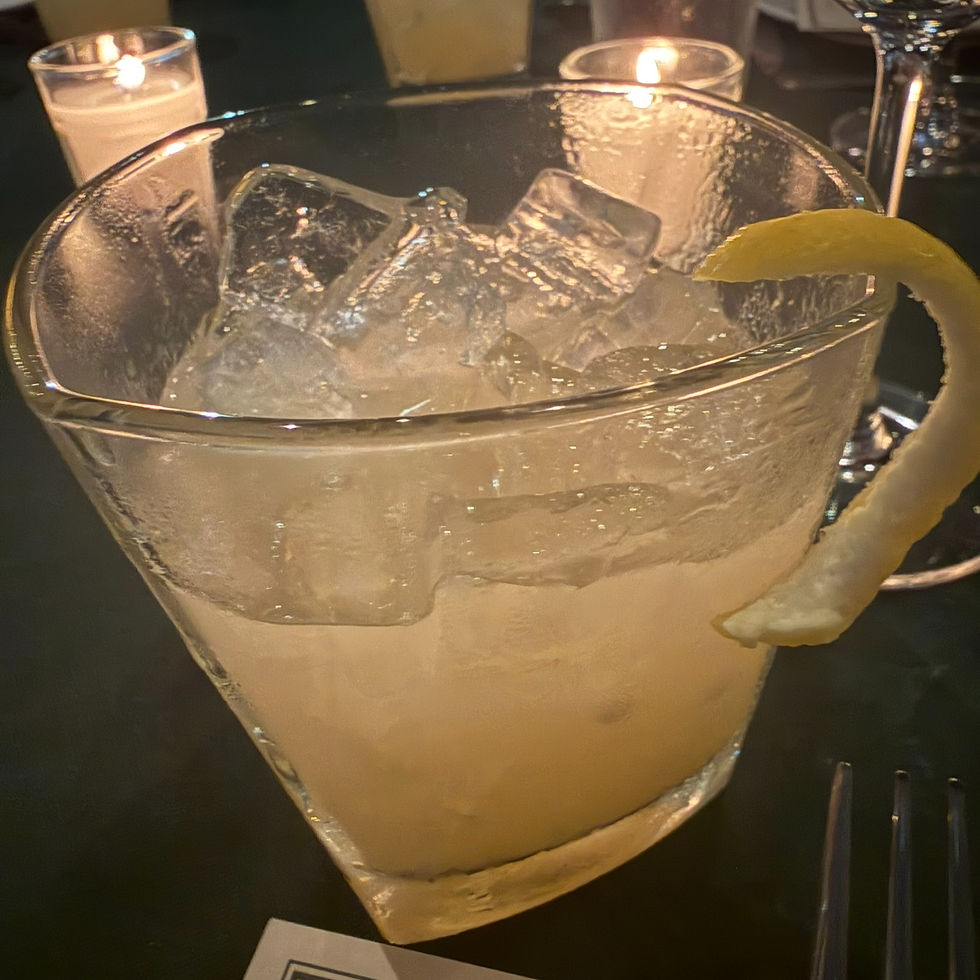 Lemon cocktail in an ice-filled glass with a lemon twist, lit candles behind it on a dim restaurant table.