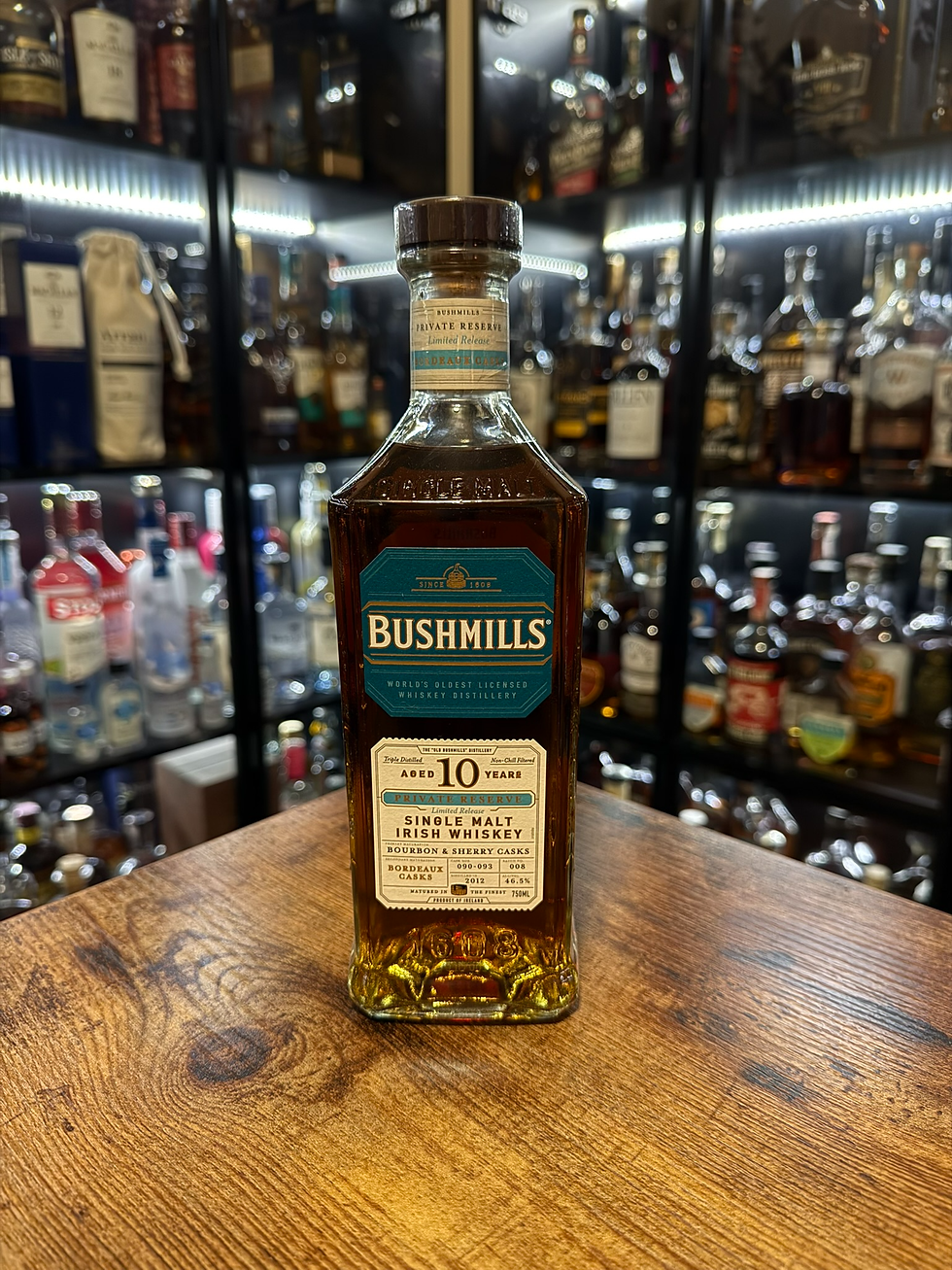 Bushmills 10-year single malt Irish whiskey bottle on a wooden table, with a blurred shelf of liquor bottles behind.