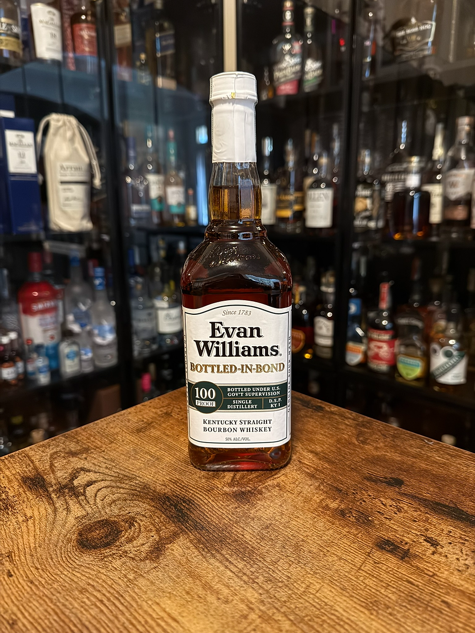 Evan Williams Bottled-In-Bond bourbon bottle on a wooden table, with liquor bottles blurred in the background.