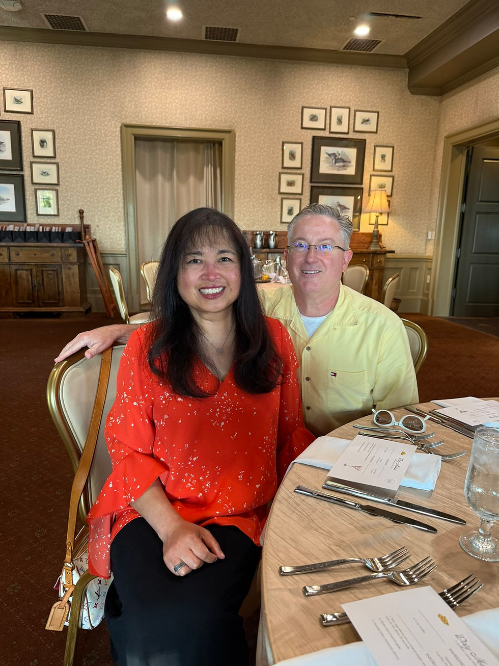 Smiling couple seated at a set dining table in a cozy restaurant, with framed art on patterned walls and warm lighting.