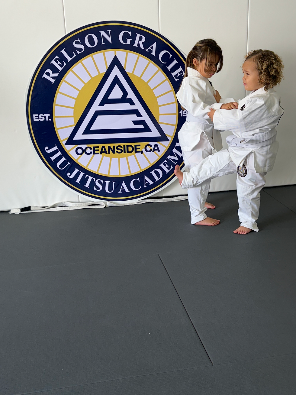 Eye-level view of a young child practicing a Jiu Jitsu hold with an instructor guiding closely