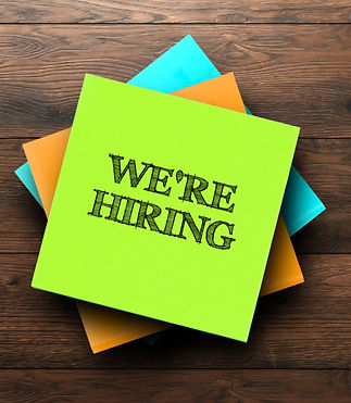 We're Hiring, the phrase is written on multi-colored stickers, on a brown wooden backgroun