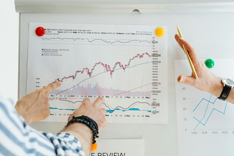 Hands point at a stock chart on a whiteboard, highlighting trends. One hand holds a gold pen. Background has colored magnets.
