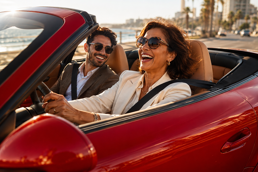 Mid-40s woman laughing with a younger man while driving a red convertible along a coastal road.
