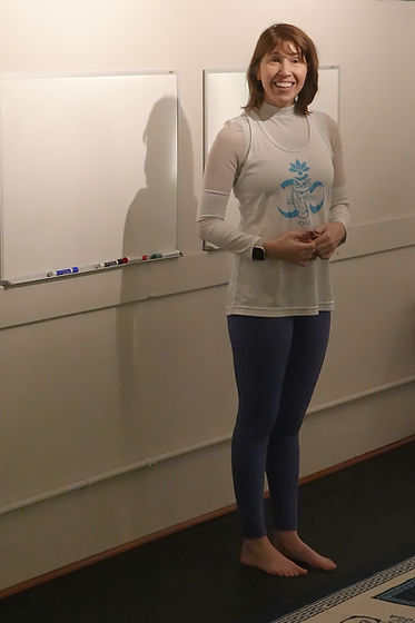Lara smiling beside the teaching board at West Wind Yoga.
