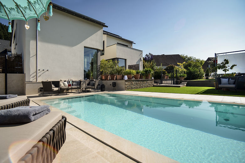 Gepflegter Garten mit verschiedenen Liegemöglichkeiten, Pflanzen und einem hellen Pool im Vordergrund.