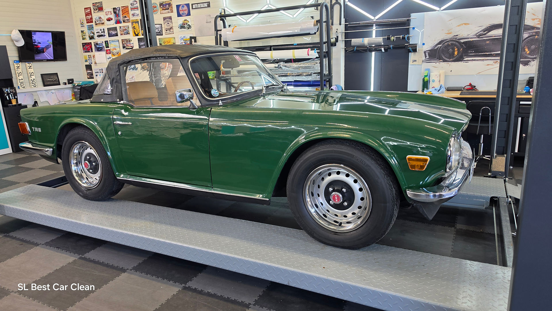 Seitenansicht eines klassischen grünen Triumph TR6 Oldtimers auf einer Hebebühne in der modern ausgestatteten Aufbereitungshalle von SL Best Car Clean, glänzender Lack und Speichenfelgen im Fokus.