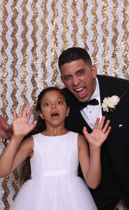 Father and daughter all dressed up posing with silly faces infront of an instant-print photo booth by Under The Umbrella