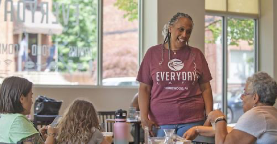 Pastor Cynthia Wallace stands before a table of women in the Everyday Cafe dining room.