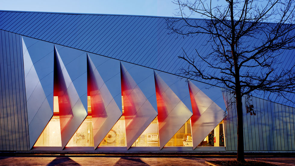 Seitenaufnahme bei Nacht der Versuchshalle an der TU Darmstadt, entworfen des Architekten Johann Eisele. Farben rot gelb, und ein Baum im Vordergrund
