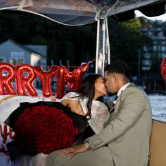 Couple kissing on boat, "Marry Me" balloons, red roses