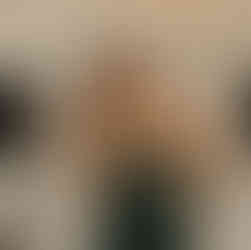 Joyful woman in green dress posing, hand in hair at event.