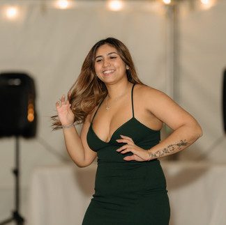 Joyful woman in green dress posing, hand in hair at event.