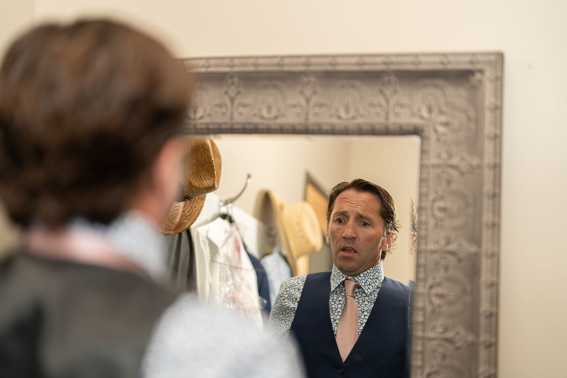 Man in vest and tie, stressed, looking at his reflection in mirror.