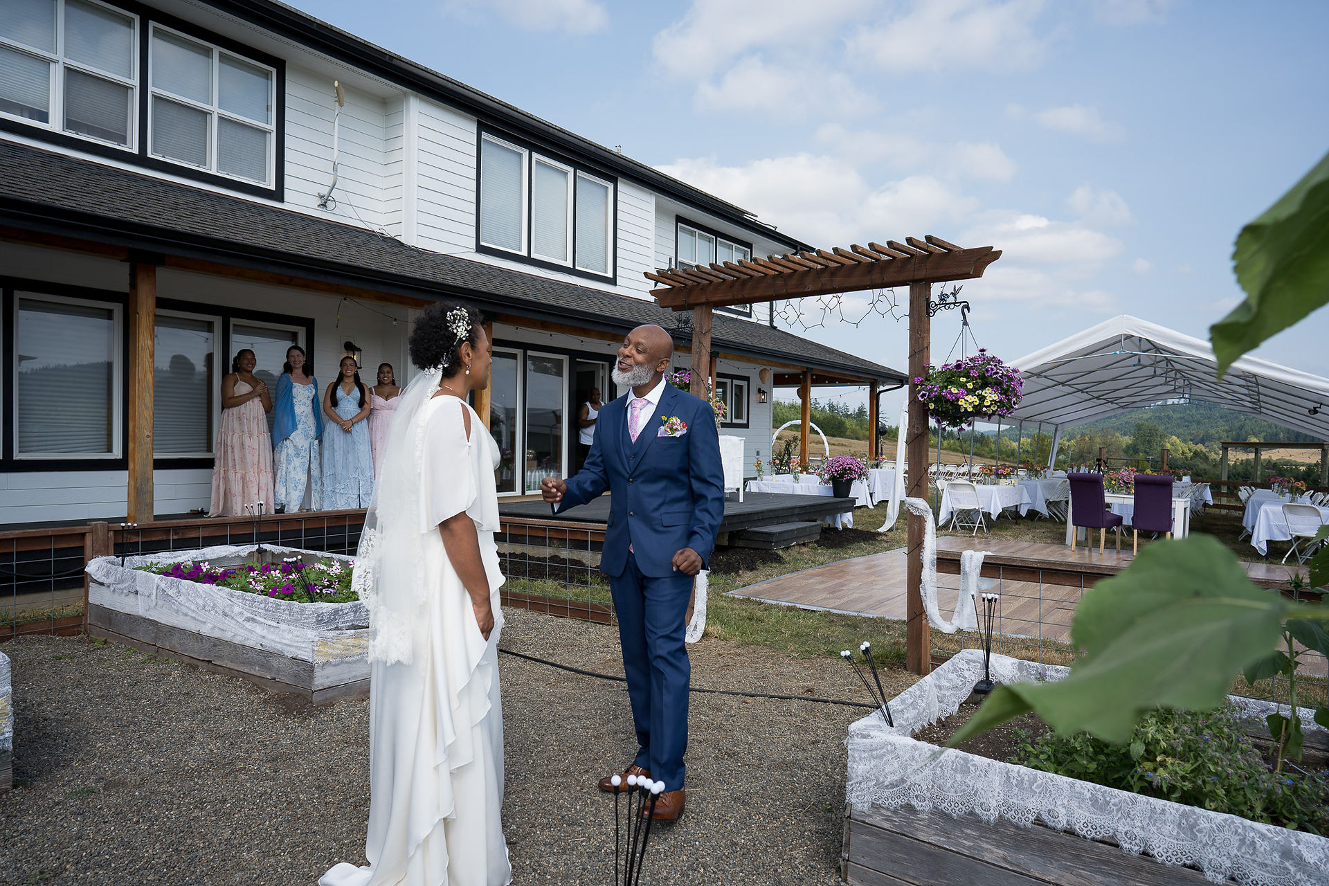 Bride and man in blue suit converse at outdoor farm wedding.