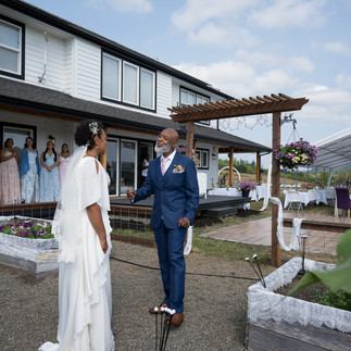 Bride and man in blue suit converse at outdoor farm wedding.