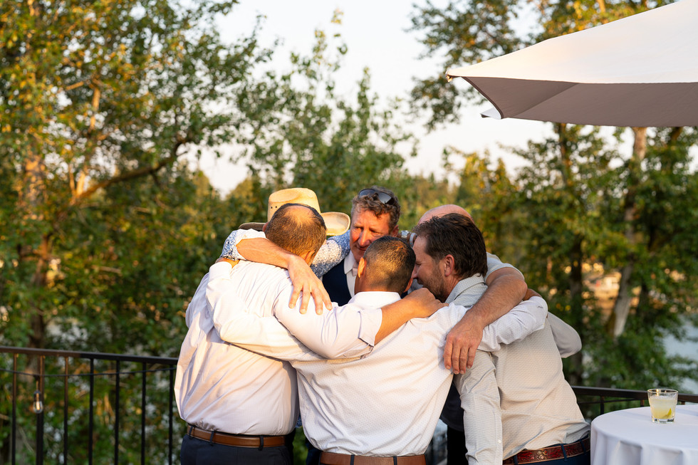Five men huddle closely in warm outdoor light, showing camaraderie.