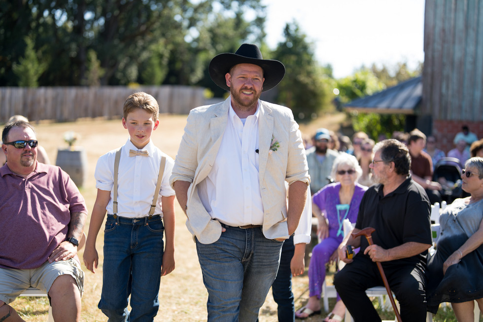 Man in cowboy hat and boy walking down aisle at outdoor wedding.