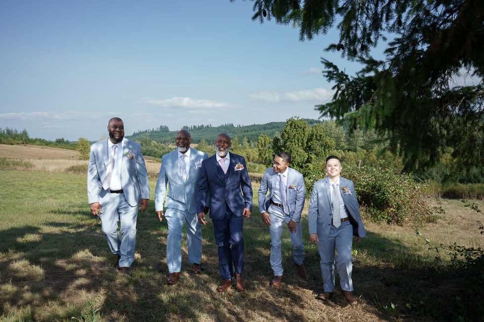 Five men in various blue suits walking outdoors for a farm wedding.