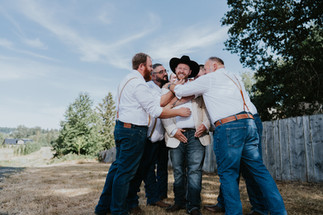 Groom and groomsmen joyfully hugging outdoors on wedding day.