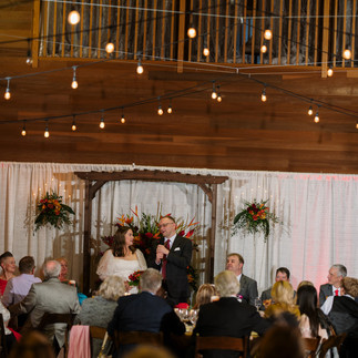 Couple gives wedding reception speech to guests under festive string lights.