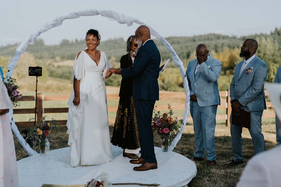 Groom placing ring on bride's finger at their rustic outdoor wedding.