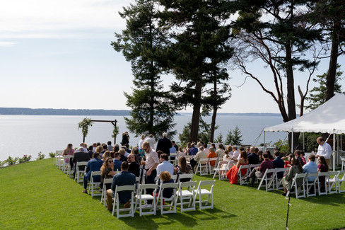 Guests seated at an outdoor wedding ceremony overlooking the water.
