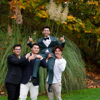 Four happy men, one on shoulders, celebrating outdoors with autumn foliage.