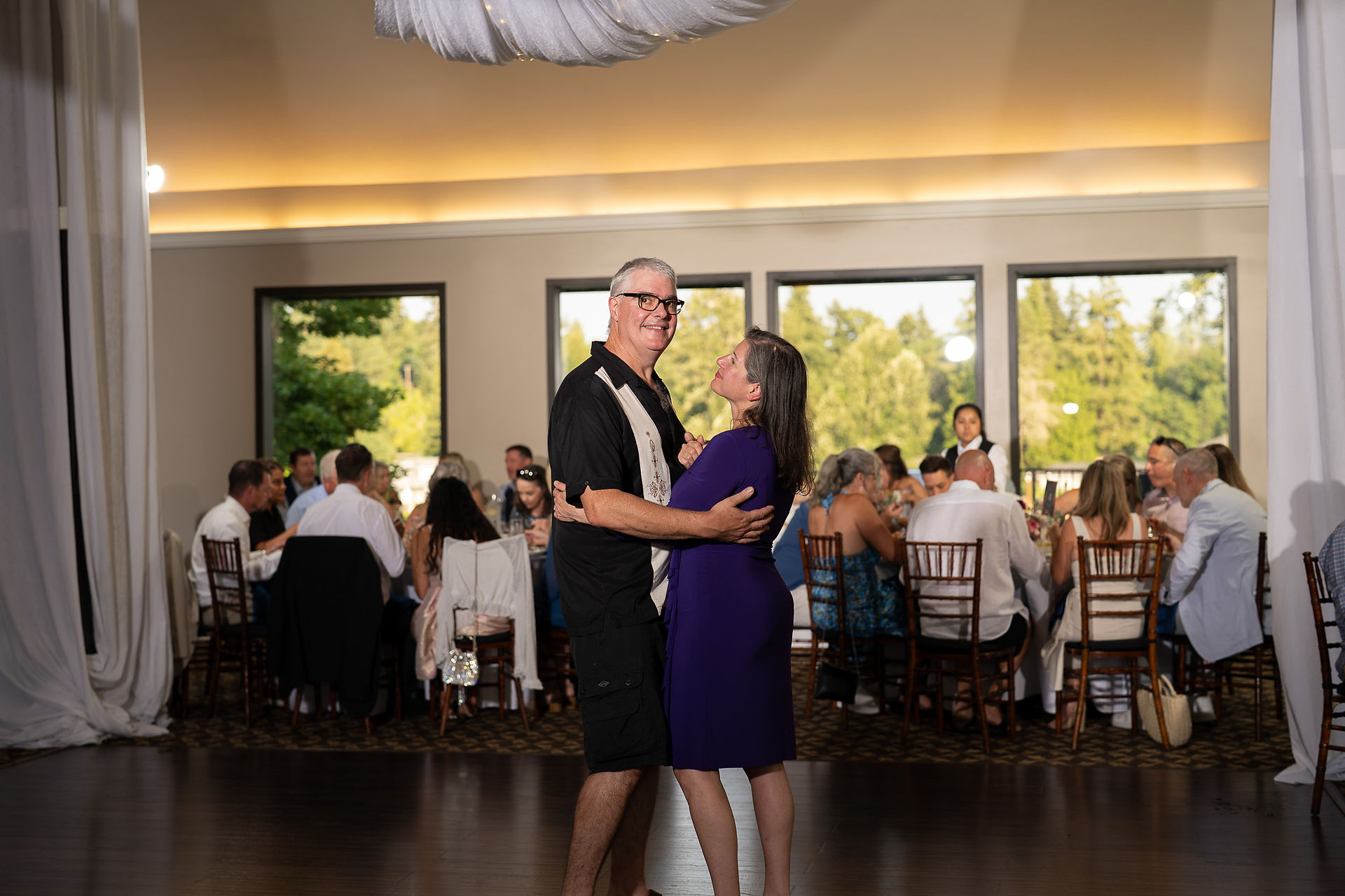 Couple dancing intimately at a lively wedding reception indoors.