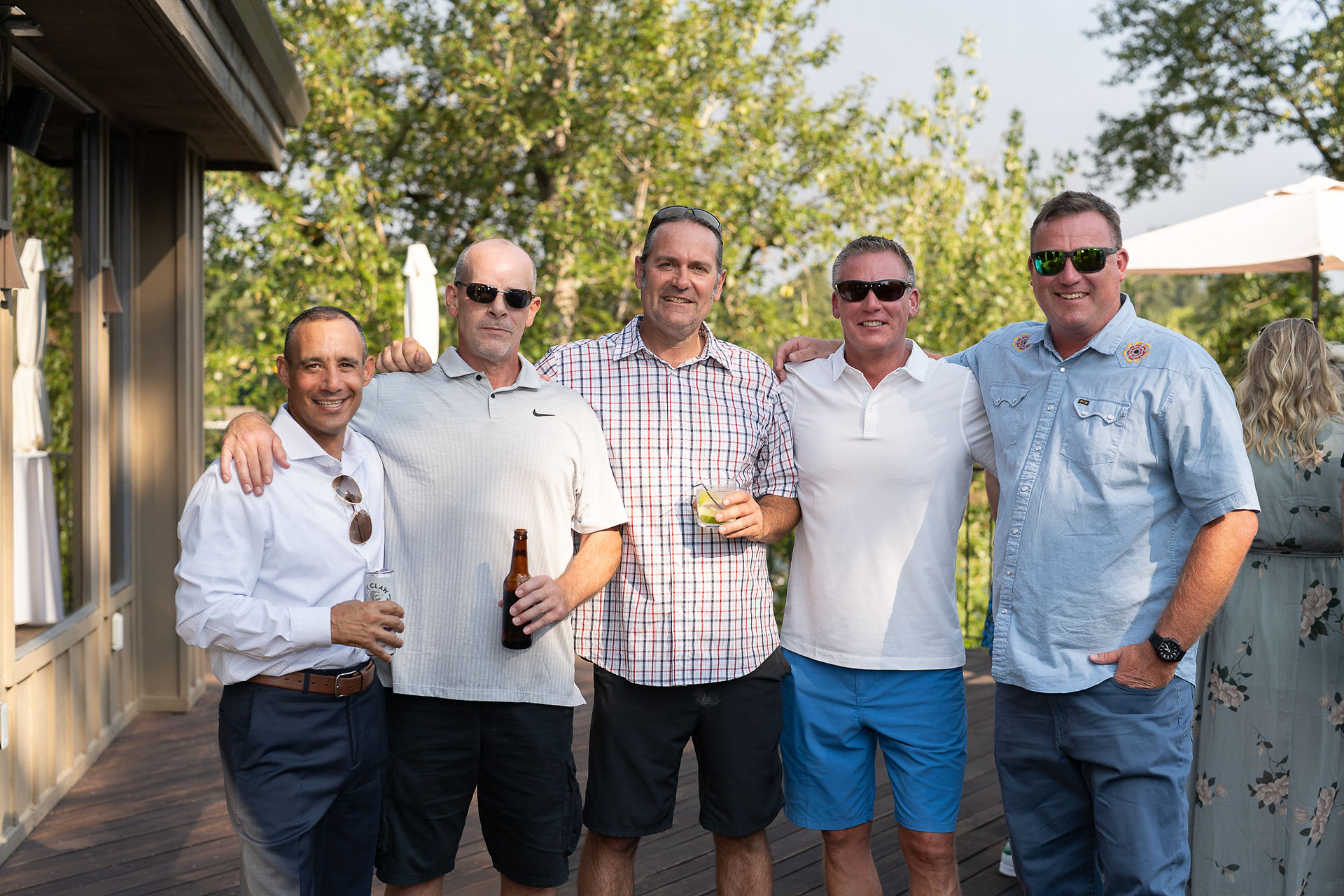Five smiling men posing outdoors at a casual gathering.