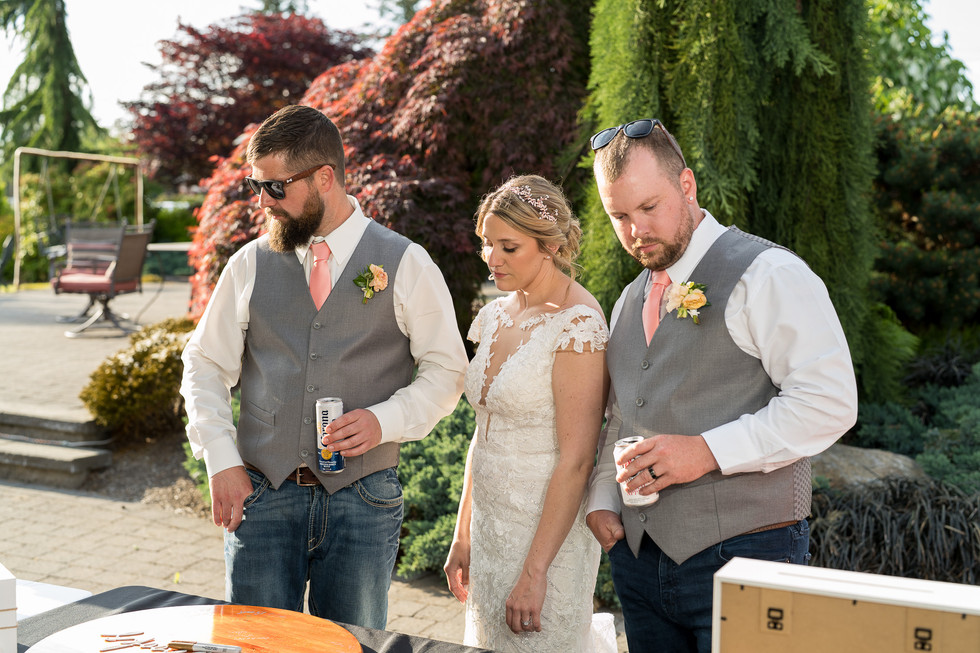 Bride and two groomsmen in vests looking down at outdoor wedding.