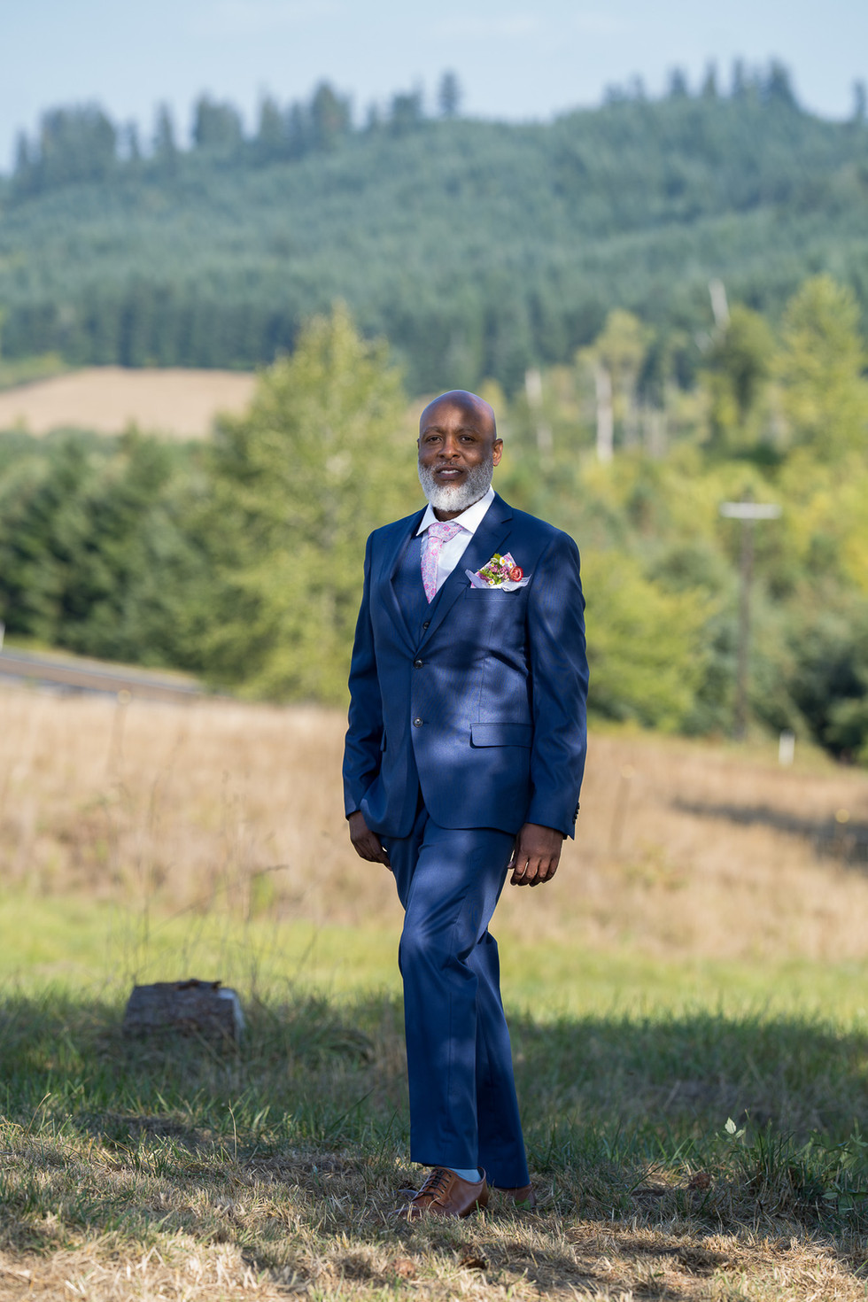 Older Black man in blue suit walking in sunny field.