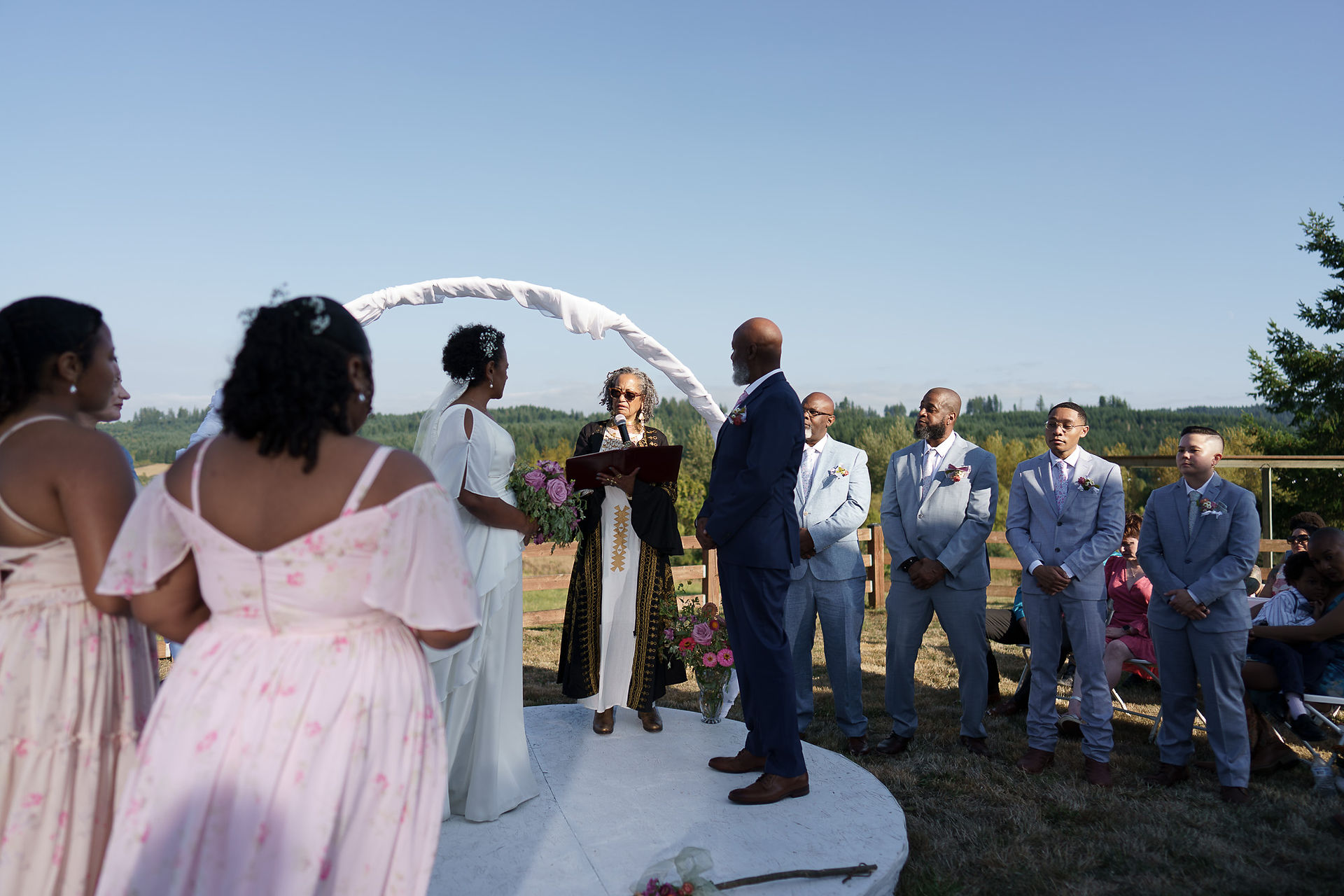 Bride and groom exchanging vows under arch, intimate farm wedding.