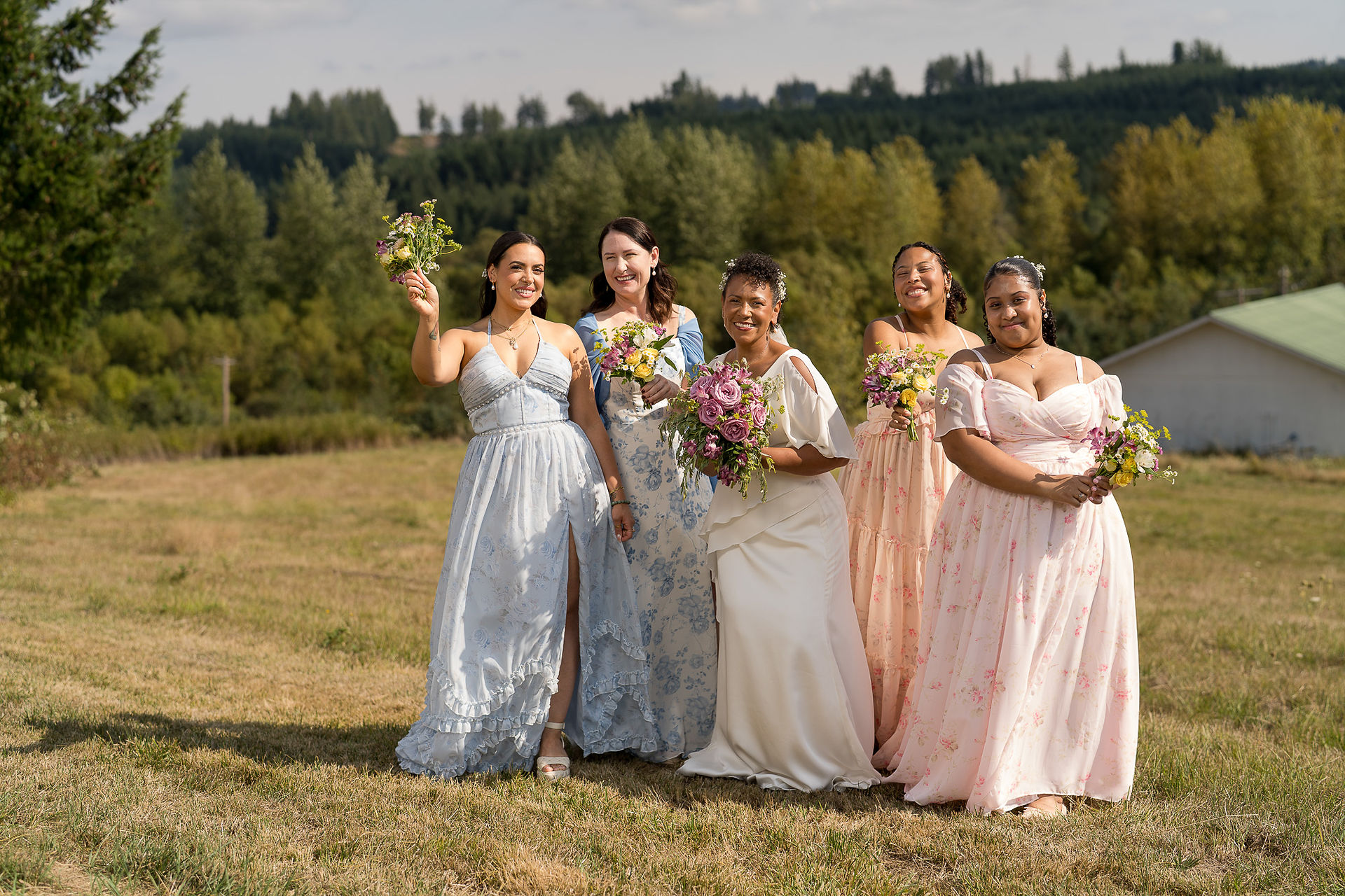 Bride and bridesmaids smiling with bouquets at an intimate farm wedding.