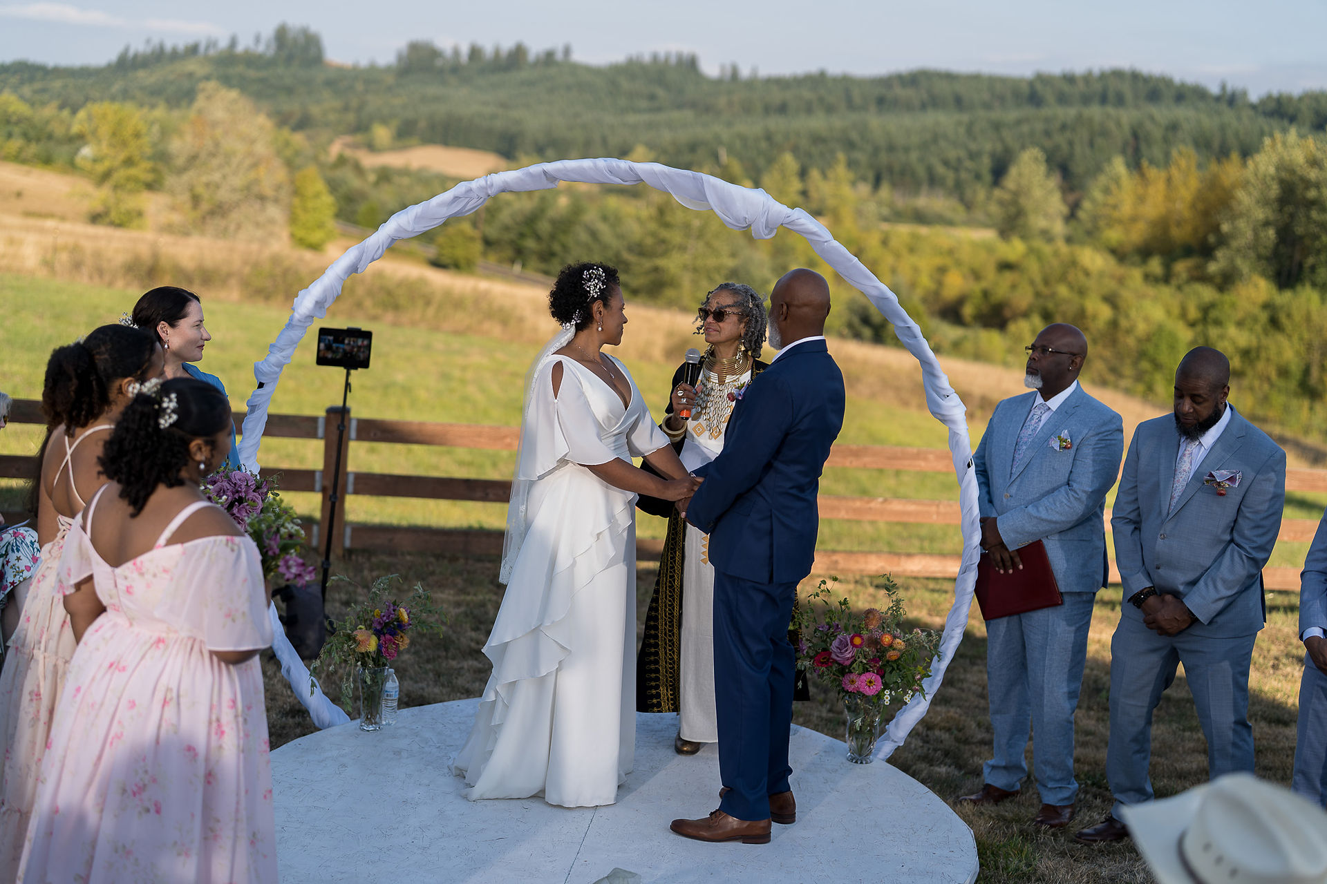 Couple exchanging vows under arch at beautiful outdoor farm wedding.