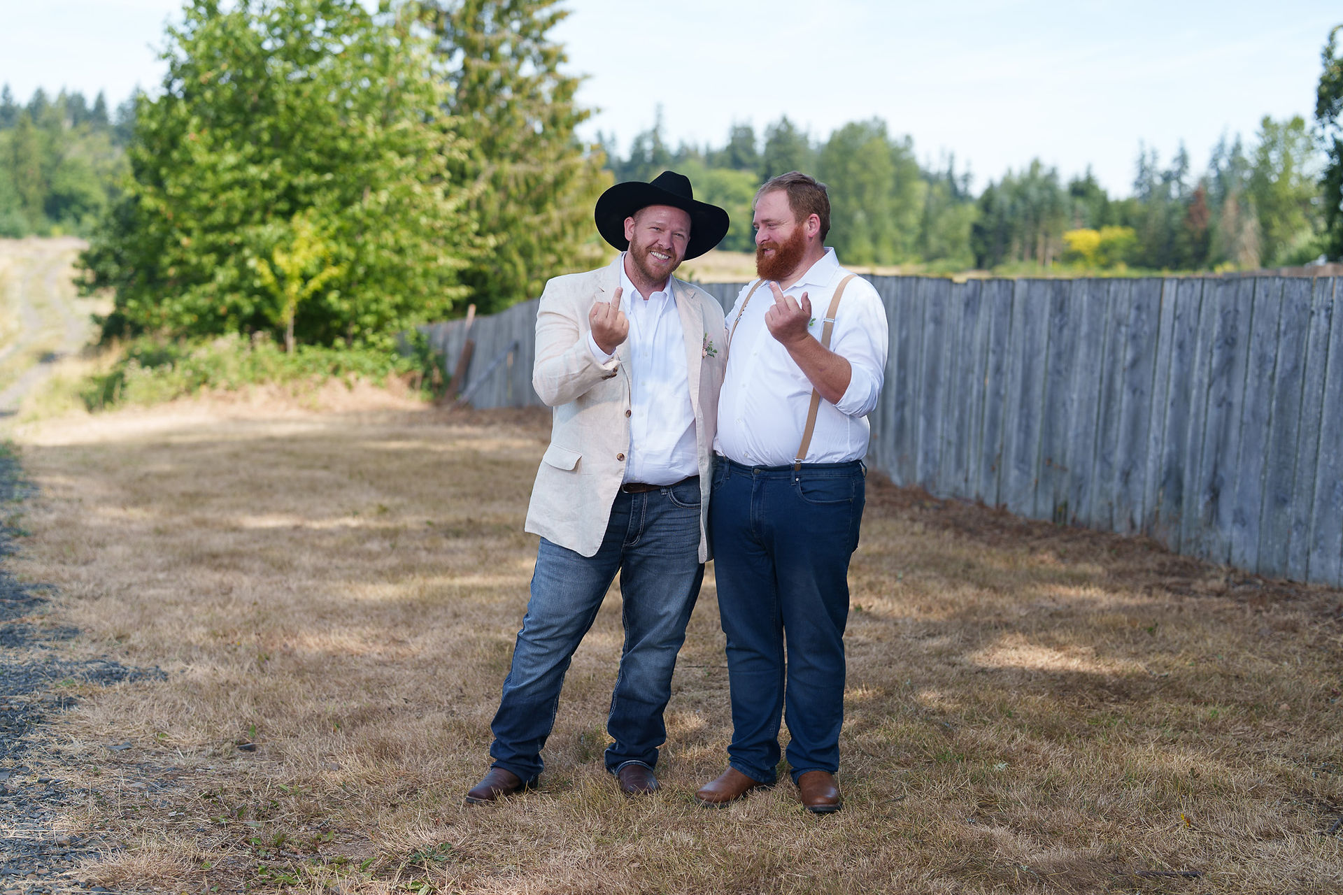 Two smiling men in wedding attire gesturing playfully outdoors.