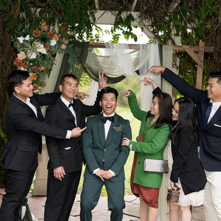 Happy groom in green suit with five smiling guests pointing.