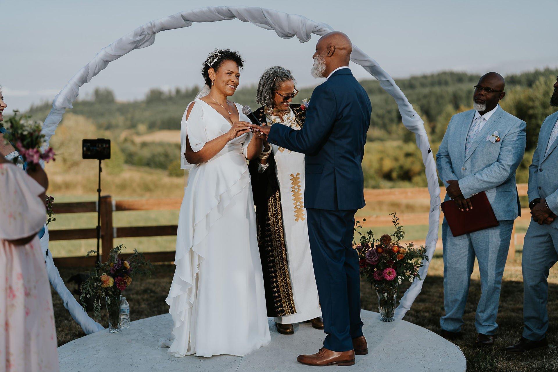 Bride and groom exchanging rings under wedding arch outdoors.