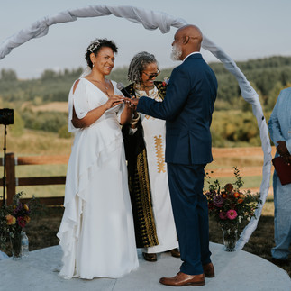 Bride and groom exchanging rings under wedding arch outdoors.