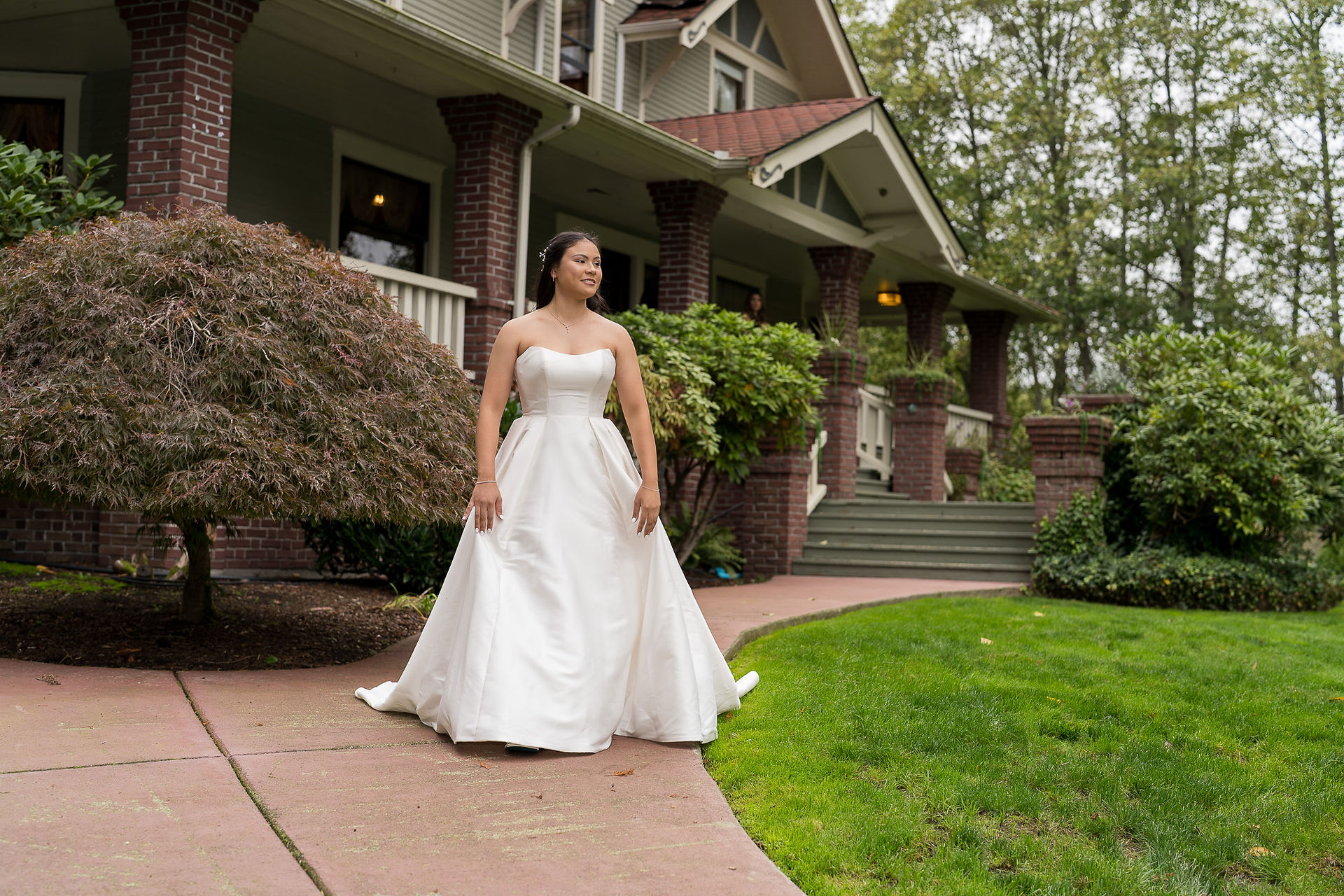 Smiling bride in white gown on path before large house porch.