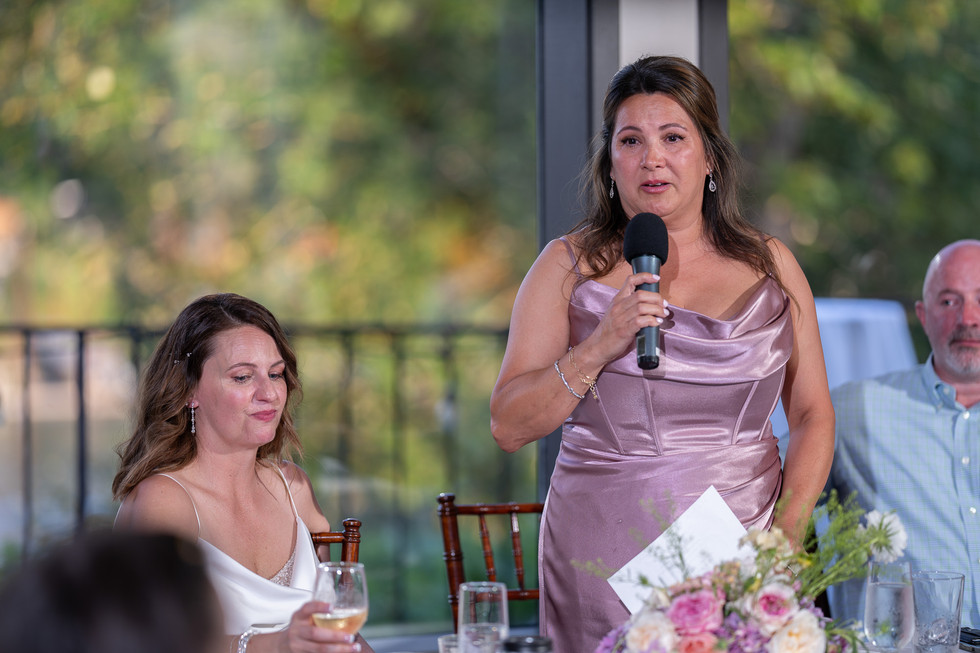 Woman in lavender dress speaking into microphone at wedding reception.