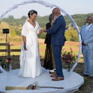 Bride and groom exchanging rings at outdoor wedding with jumping broom.