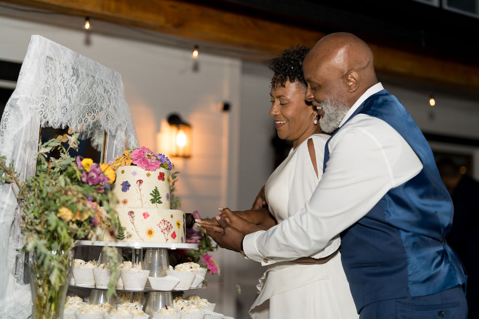 Diverse couple cutting whimsical wedding cake at intimate farm wedding.