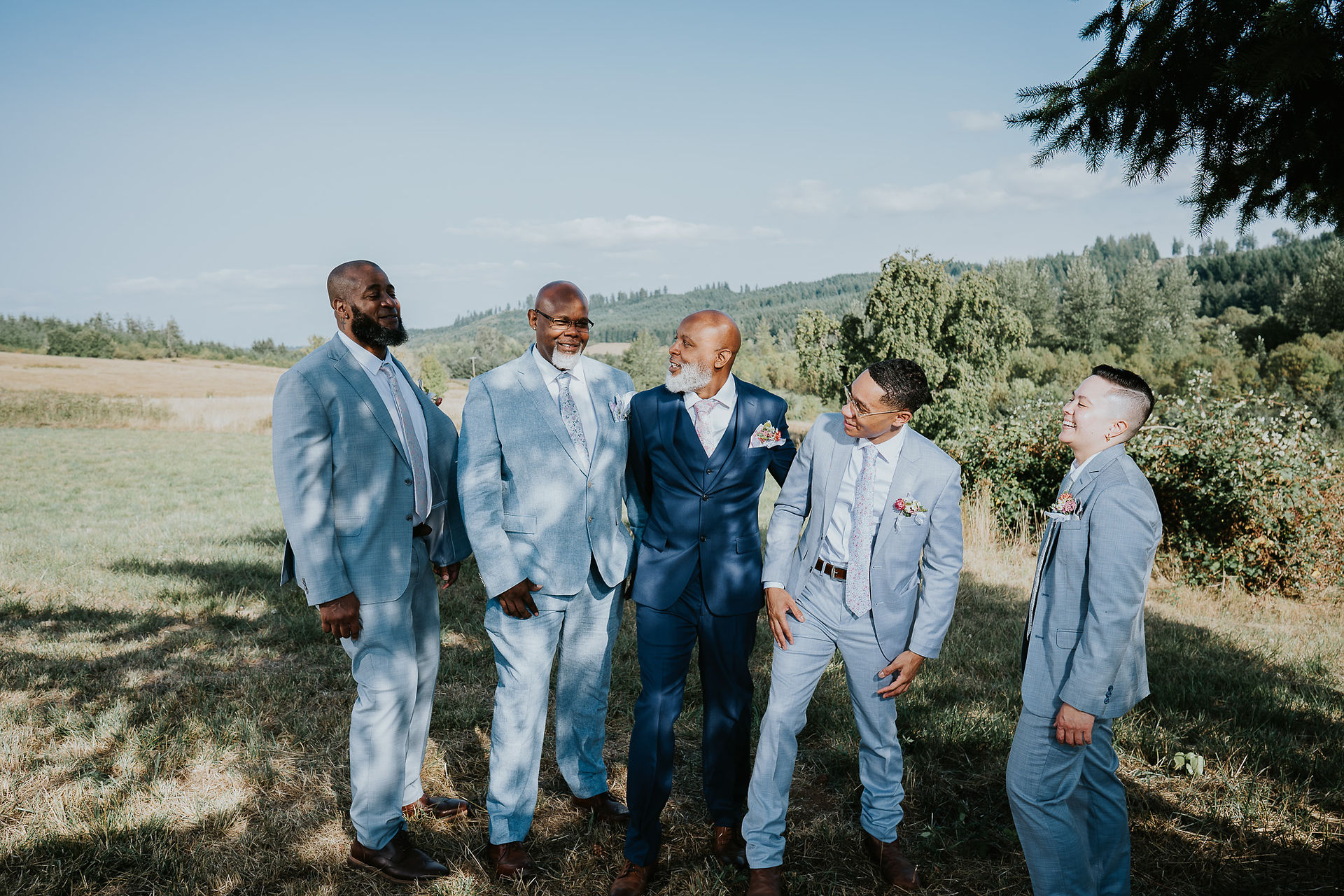 Smiling groomsmen in blue suits outdoors, celebrating an intimate farm wedding.