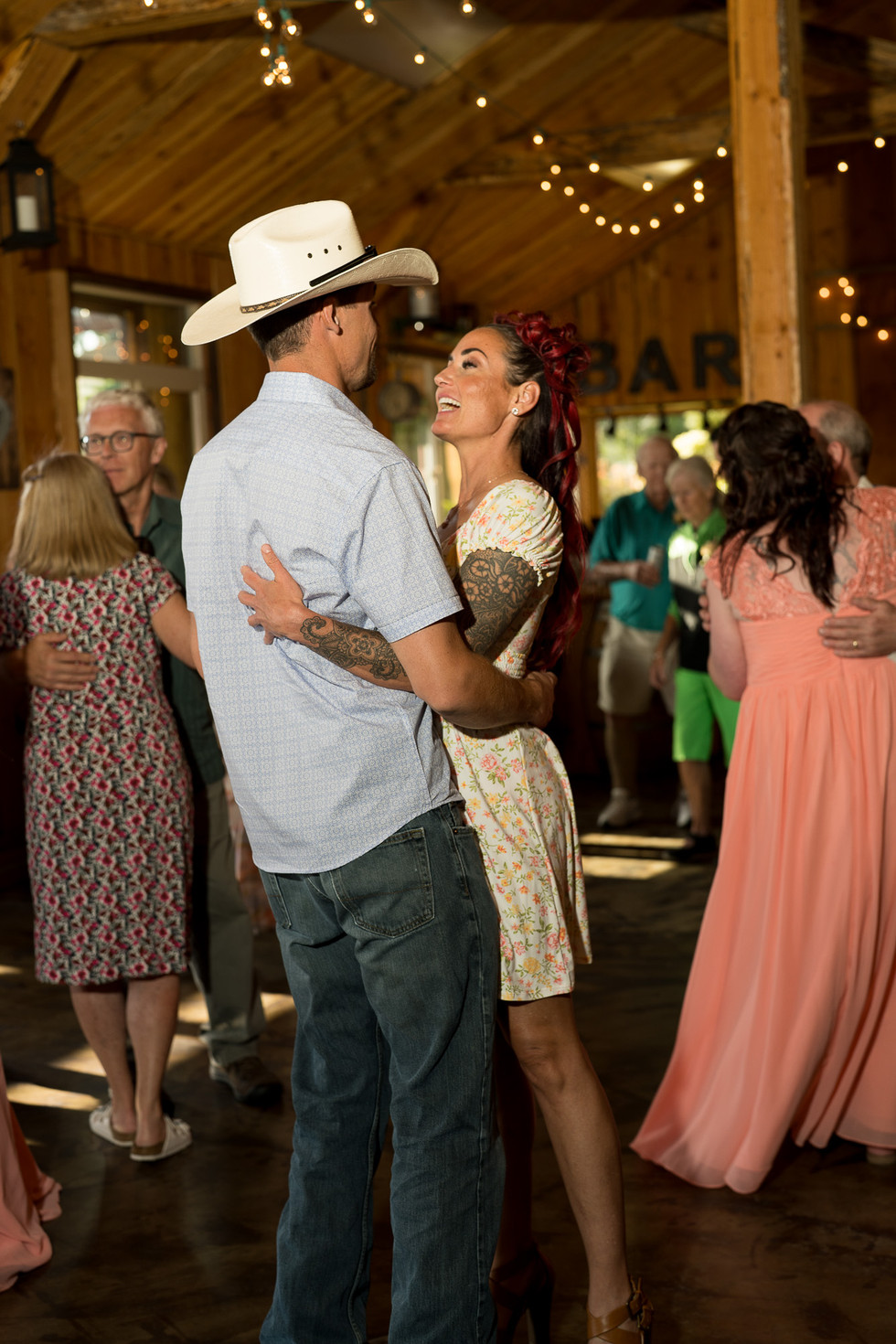 Couple dancing intimately at a rustic wedding reception, with "BAR" sign.