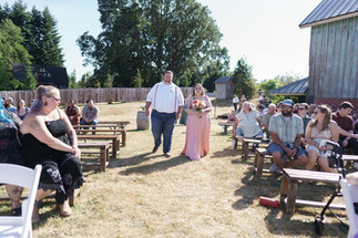 Couple walking down outdoor wedding aisle, guests watching.
