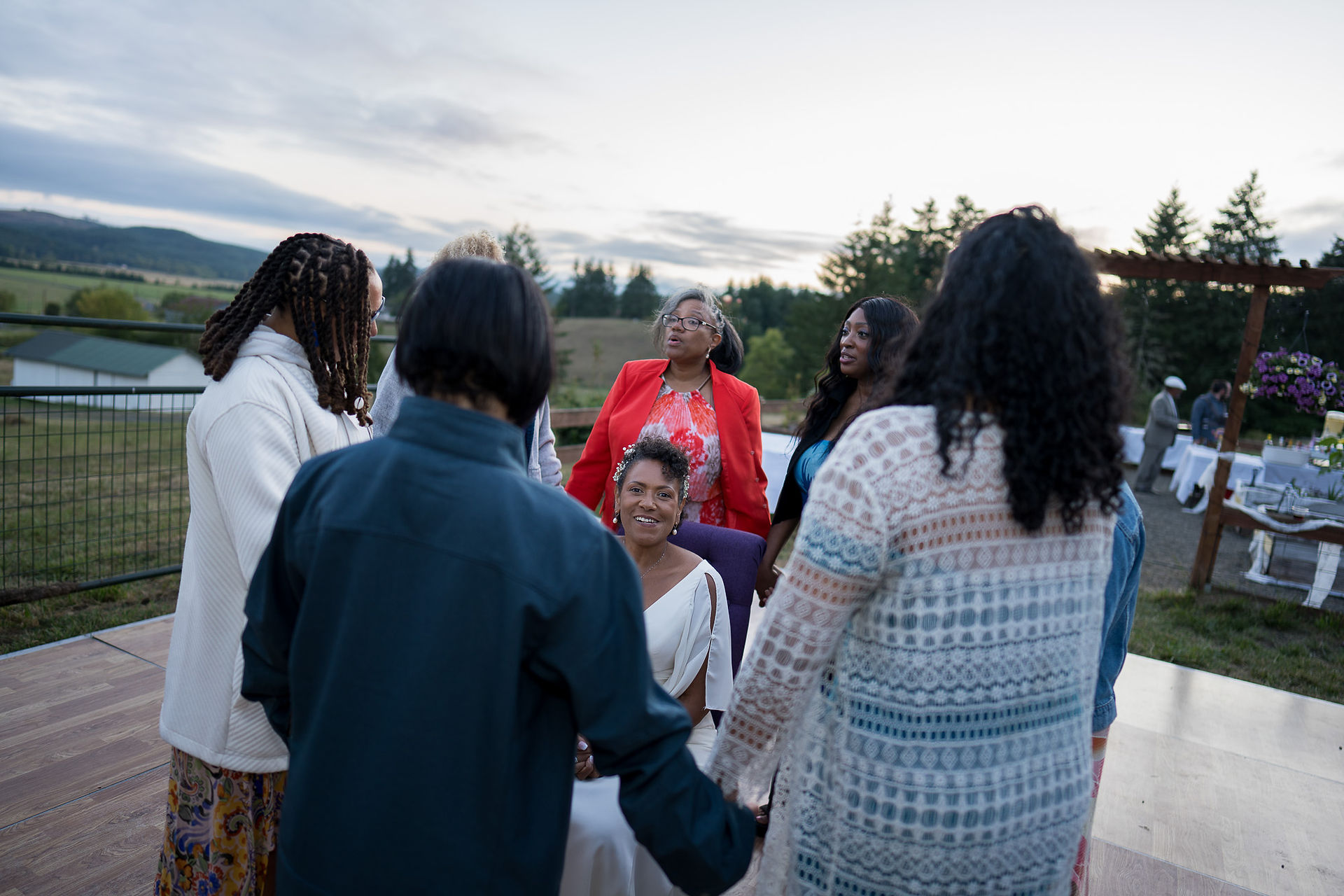 Diverse women gathered outdoors in a circle, holding hands, smiling.