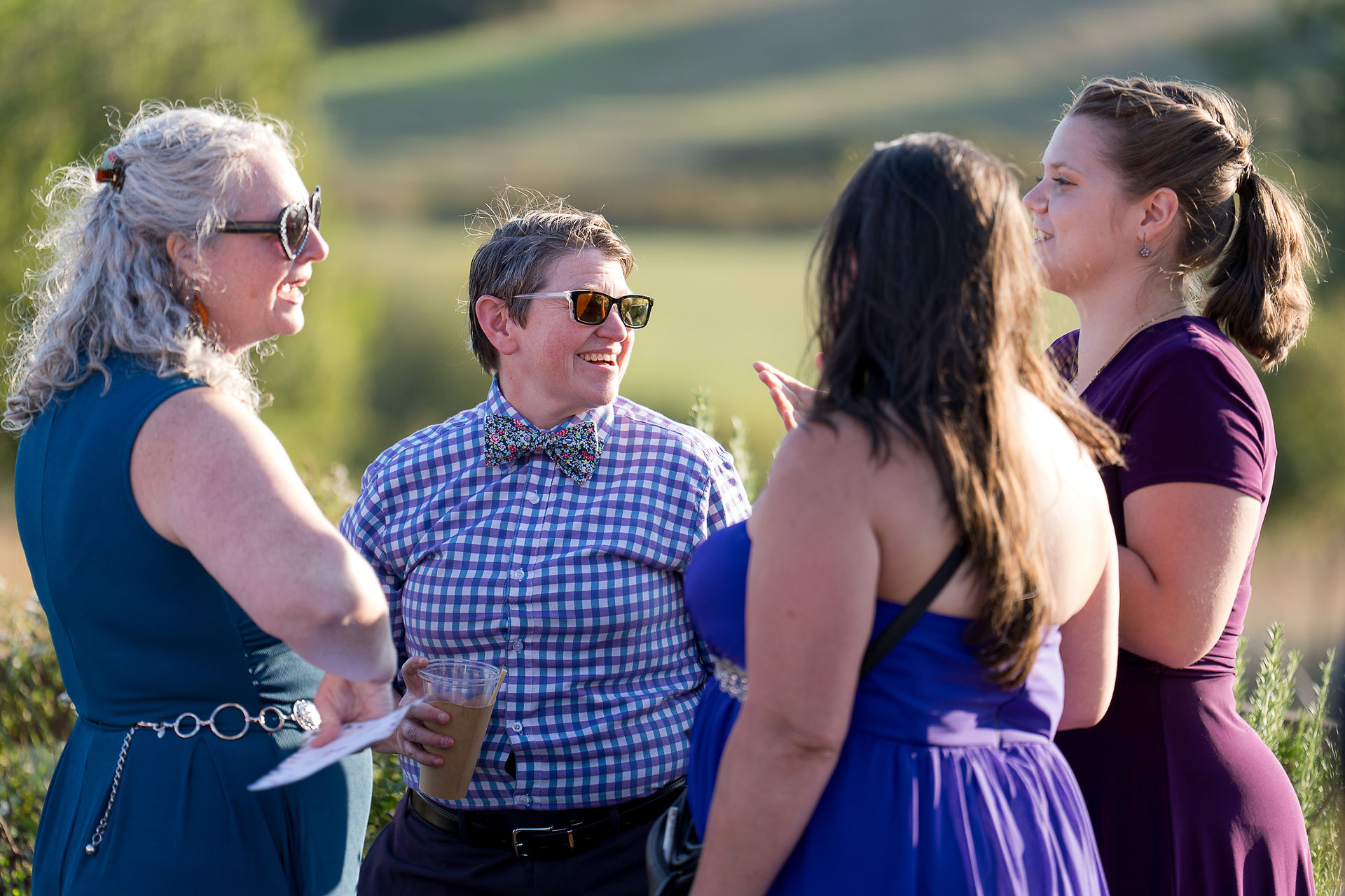 Guests conversing happily outdoors, person in bow tie and sunglasses smiling.