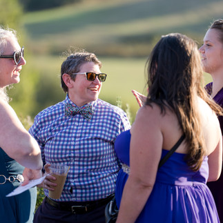 Guests conversing happily outdoors, person in bow tie and sunglasses smiling.