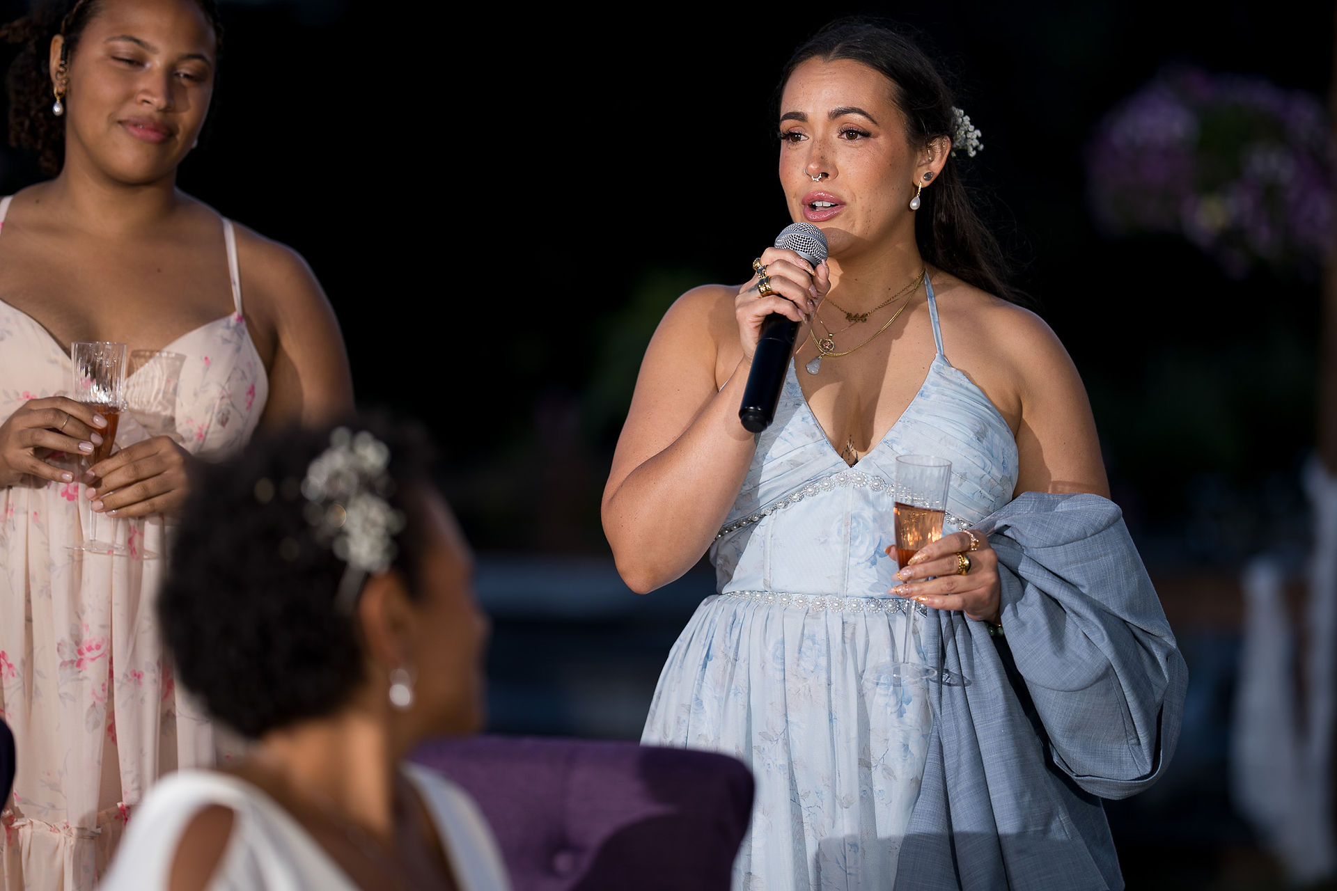 Young woman gives speech holding microphone and champagne glass at reception.
